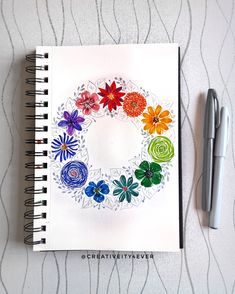 a spiral notebook with flowers on it next to a pen