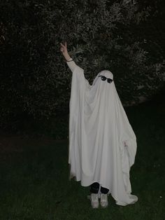 a person dressed in a ghost costume standing on the grass with their arms outstretched up