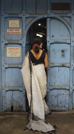 a woman standing in front of a blue door wearing a white and black sari