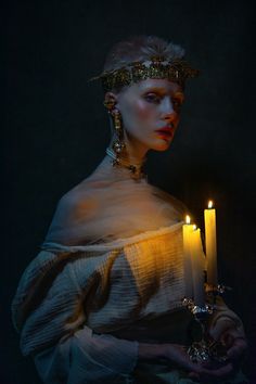 a woman holding a candle in her hand and wearing a head piece with gold jewelry