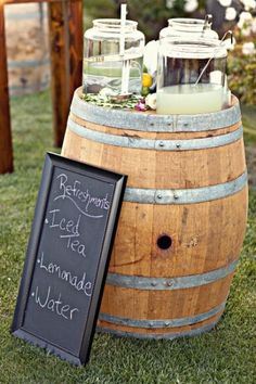 a wooden barrel sitting on top of a lush green field next to a chalkboard sign