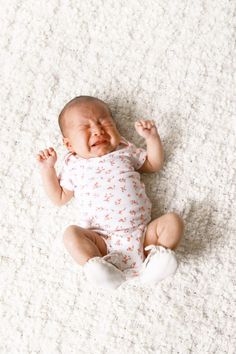 a baby crying while laying on the floor with his hands up and eyes wide open