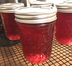 four jars filled with red liquid sitting on top of a metal grate covered counter