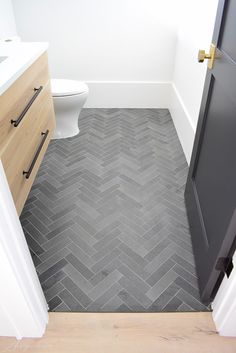 a bathroom with grey herringbone flooring and wooden cabinetry next to the toilet