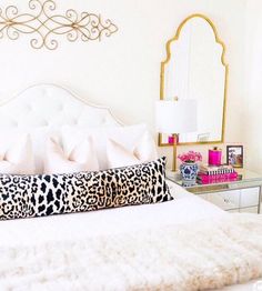 a white bed topped with lots of pillows next to a wall mounted mirror and lamp