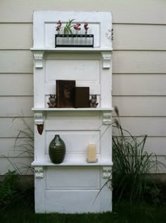 a shelf with books and vases on it in front of a white house next to grass