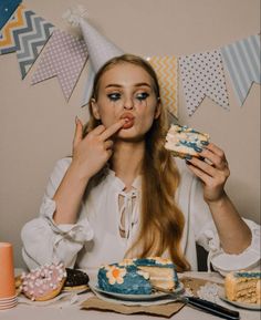 a woman sitting at a table with a cake in front of her face and party decorations around her