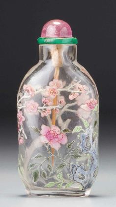 a glass bottle with flowers painted on the side and a green top, sitting on a gray surface