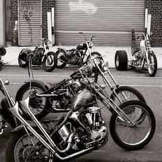 black and white photograph of three motorcycles parked in front of a building with garage doors