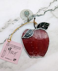 an apple shaped keychain with a tag attached to it on a marble surface