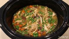 a crock pot filled with chicken, peas and carrots on top of a table