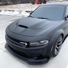 the front end of a black car parked in a parking lot with snow on the ground