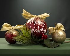 two christmas ornaments with bows and ribbons on a green tablecloth, next to the words merry christmas