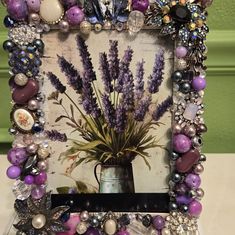 a picture frame decorated with beads and lavenders on a white table top next to a green wall