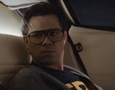 a man wearing glasses sitting in the back seat of a car with his head turned to the side