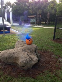 a fake pumpkin sitting on top of a rock in the middle of a yard next to a fire hydrant