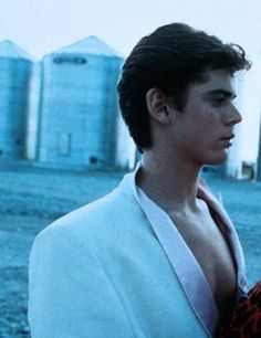 a young man in a white suit and red scarf standing next to a barn with silos