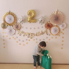 a young boy standing next to a green bag in front of a wall with gold and silver decorations