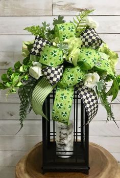 a green and white bow on top of a birdcage filled with greenery