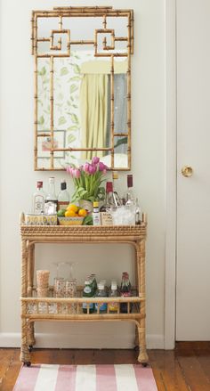 a bamboo bar cart with drinks on it in front of a mirror and striped rug