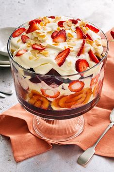 a trifle with strawberries and cream in a glass dish on an orange napkin