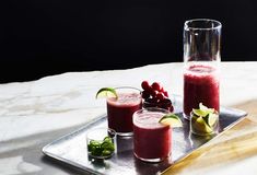 three glasses filled with different types of drinks on a tray next to a knife and some fruit