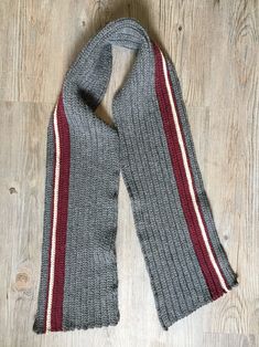 a gray scarf with red and white stripes is laying on a wooden floor next to a pair of scissors