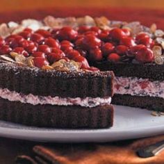 a chocolate cake with cherries and nuts on top is sitting on a white plate