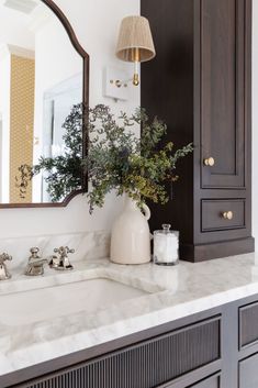 a bathroom with marble counter tops and dark wood cabinets, along with a white vase filled with greenery