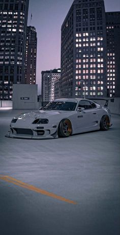 a white sports car parked in an empty parking lot with skyscrapers in the background