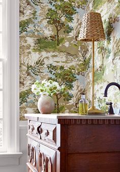 an antique dresser with a lamp on it in front of a wallpapered room