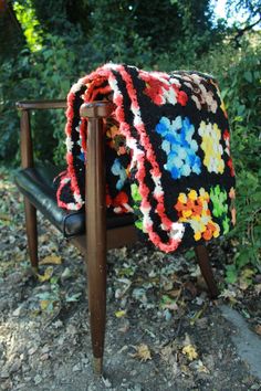 a crocheted blanket sitting on top of a wooden chair next to trees and leaves