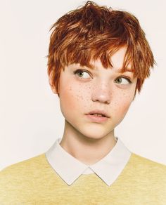 a woman with freckles on her face looks at the camera while wearing a sweater