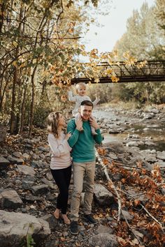 a man, woman and child are standing on rocks in the woods near a river