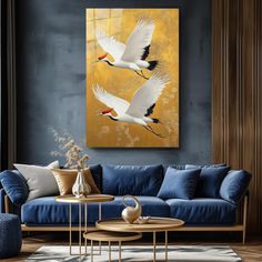 two white birds flying over a blue couch in a living room with yellow and gray walls