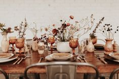 a wooden table topped with lots of plates and vases filled with flowers on top of it