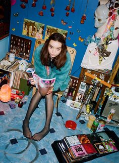 a young woman sitting on the floor reading a magazine in her room with many clutter