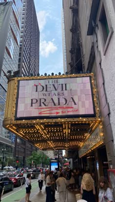 people walking on the sidewalk in front of a theater sign that says devil is pira