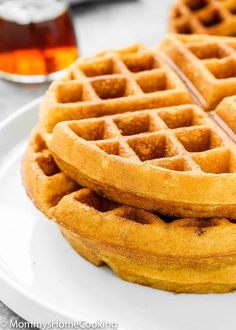 three waffles stacked on top of each other on a plate with syrup in the background