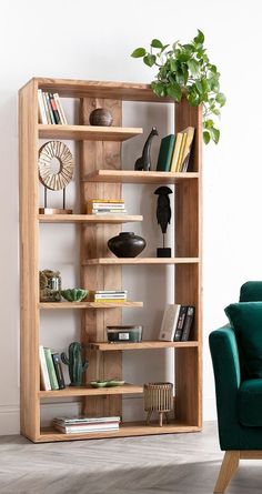 a green chair sitting in front of a wooden book shelf filled with books and plants