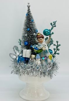 a small christmas tree in a white bowl with silver tinsel and blue ornaments on it