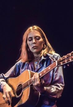 a woman with long hair playing an acoustic guitar