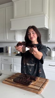 a woman standing in front of a cutting board with chocolate cake on top of it