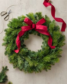 a christmas wreath with red ribbon and scissors on a table next to some other holiday decorations