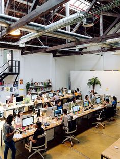 there are many people sitting at desks in this large room with computers on them