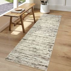 a wooden bench sitting next to a white rug on top of a hard wood floor