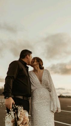 a bride and groom kissing in an empty parking lot with the sun setting behind them