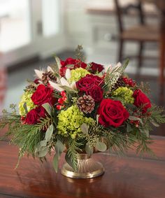 a vase filled with red and green flowers on top of a wooden table