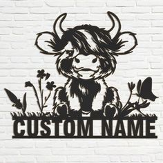 a metal sign that says custom name with a cow sitting in the grass and flowers