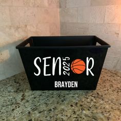 a black basket with the words senior and an orange basketball in it on a granite countertop